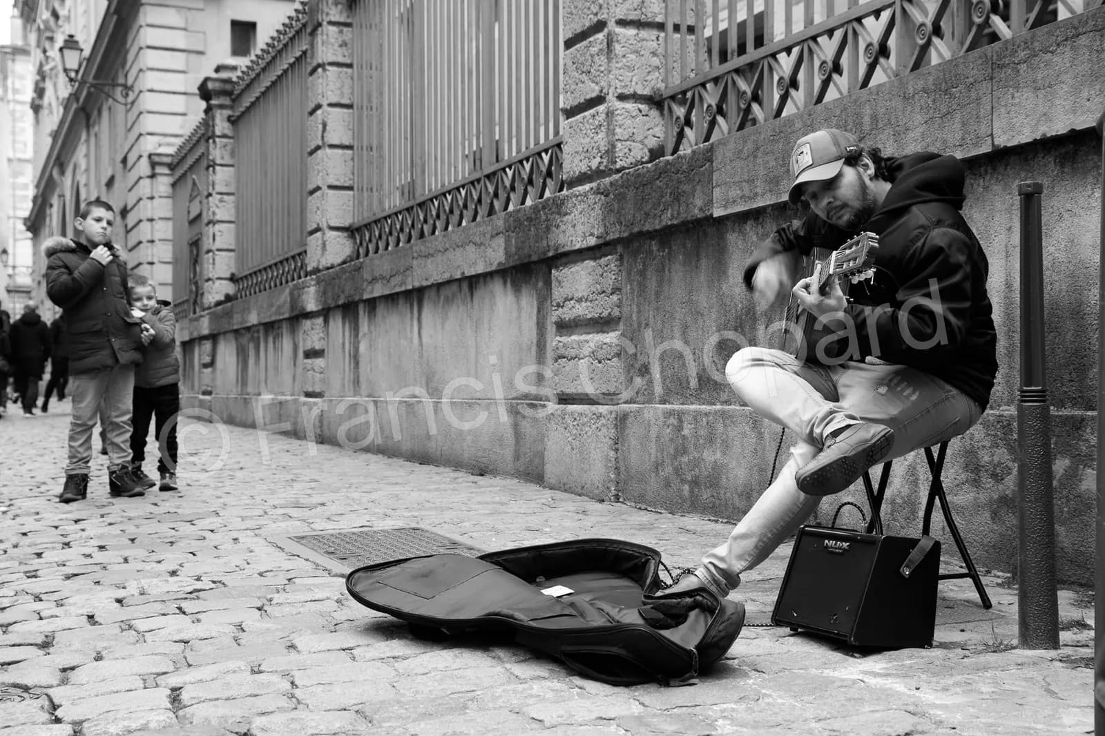 Deux enfants regardent un guitariste dans une rue pavée